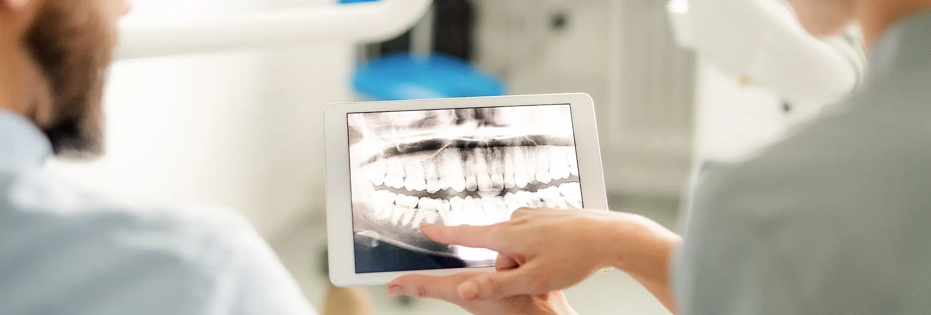 Zahnarzt zeigt Patientin ein digitales Röntgenbild der Zähne auf einem Tablet
